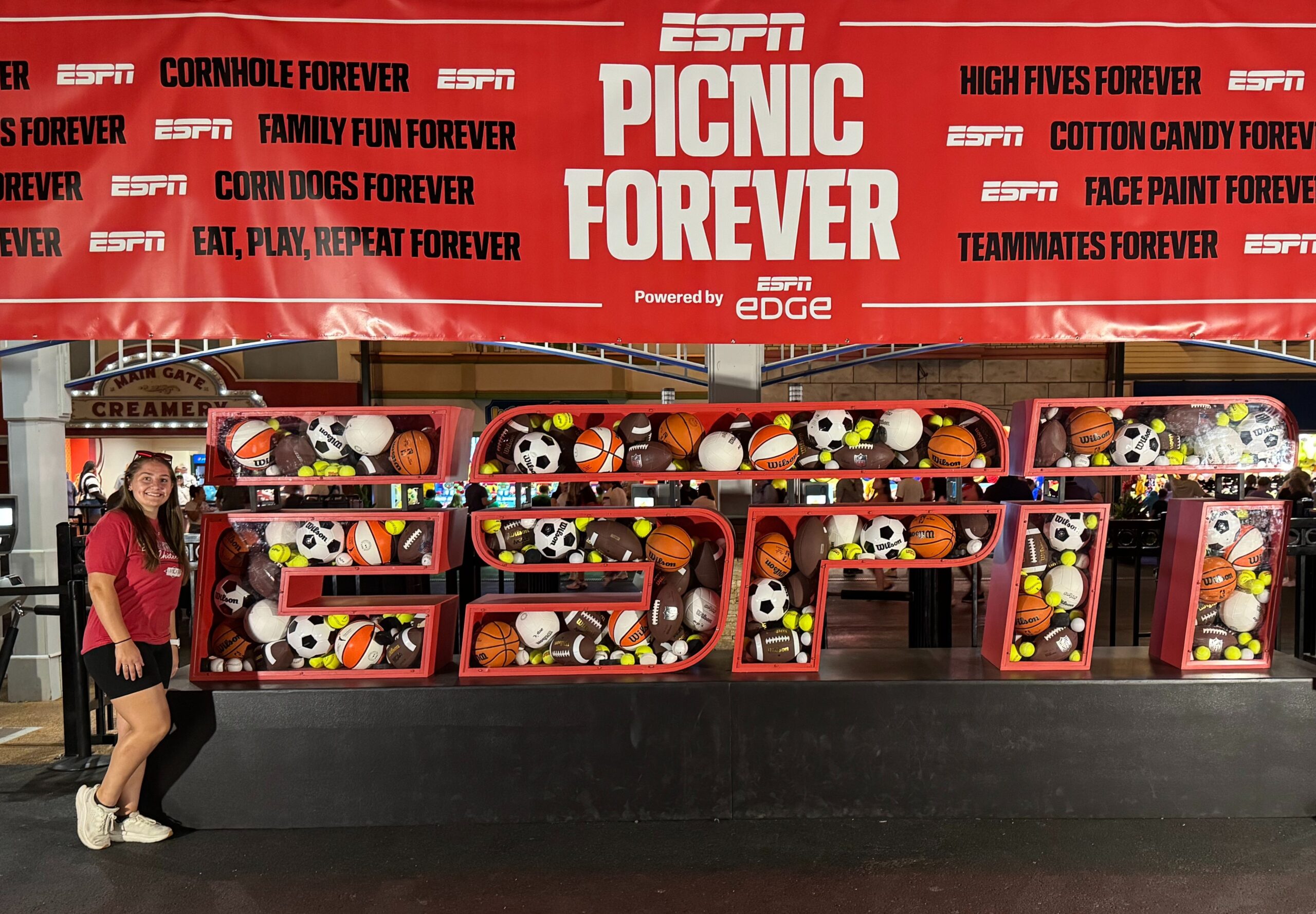 A young woman stands in front of a red, white, and black banner that says ESPN Picnic Forever